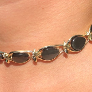 May include: A gold chain necklace with black oval-shaped stones. The necklace is made of a delicate chain with a twisted design.