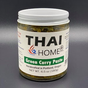 May include: A glass jar of Thai Home Green Curry Paste with a white lid. The label reads "Green Curry Paste" and "Handcrafted in Portland, Oregon." The net weight is 6.5 oz (180g).
