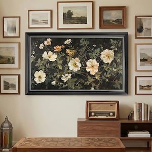 May include: A living room scene featuring a large floral painting with a black frame, surrounded by smaller framed landscape art. A wooden coffee table with a geometric design sits on a white rug. A vintage radio and decorative lanterns add to the room's aesthetic.