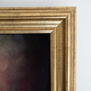 Puede incluir: Primer plano de un marco dorado con un diseño detallado y texturizado. El marco tiene un estilo clásico y ornamentado y rodea un lienzo oscuro. El marco está sobre un fondo blanco.