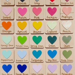 May include: Wooden color chart with acrylic heart-shaped color samples. The chart includes a variety of colors, such as red, pink, green, blue, and purple, with each color labeled with its name. The text "Acrylic Colors" is at the top.