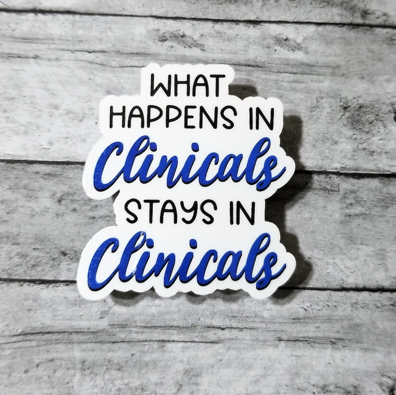 May include: A white sticker with the text "WHAT HAPPENS IN Clinicals STAYS IN Clinicals" in black and blue lettering. The sticker is on a gray wooden surface.