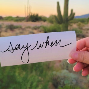 May include: A white piece of paper with the words "Say When" written in black cursive.