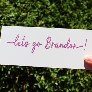May include: A white card with the text "lets go Brandon!" written in pink cursive.