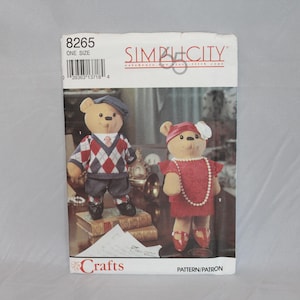 May include: A Simplicity 8265 sewing pattern envelope for stuffed bears. The cover features two bears: one wearing a grey cap, a red and white argyle sweater vest, and grey shorts; the other wearing a red hat with a white flower and a red dress.