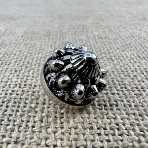 Könnte beinhalten: Ein silberner Ring mit einem detaillierten Design aus einer Ansammlung kleiner, abgerundeter Formen. Der Ring ist aus Metall und hat eine strukturierte Oberfläche.