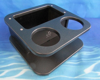 May include: Black plastic drink holder with two cup holders and a rectangular storage compartment. The holder has a textured surface and is designed to be mounted on a boat or other surface.