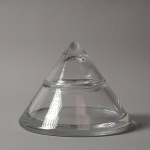 The Isolated Geometry. This fourth image, set against a neutral grey background, allows the object's formal properties to be studied without the distraction of a warm wood grain. The cool lighting emphasizes the crystal’s bluish-white refraction, a characteristic often associated with high-quality European lead crystal. From this angle, the piece ceases to be a container and becomes a study in mathematical volume.