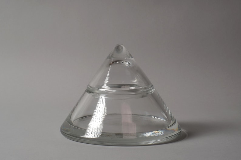 The Isolated Geometry. This fourth image, set against a neutral grey background, allows the object's formal properties to be studied without the distraction of a warm wood grain. The cool lighting emphasizes the crystal’s bluish-white refraction, a characteristic often associated with high-quality European lead crystal. From this angle, the piece ceases to be a container and becomes a study in mathematical volume.