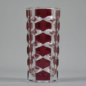 May include: A clear glass vase with a geometric design. The vase features a repeating pattern of red diamond shapes, creating a striking visual effect. The vase is cylindrical and stands upright, showcasing its decorative and functional design.