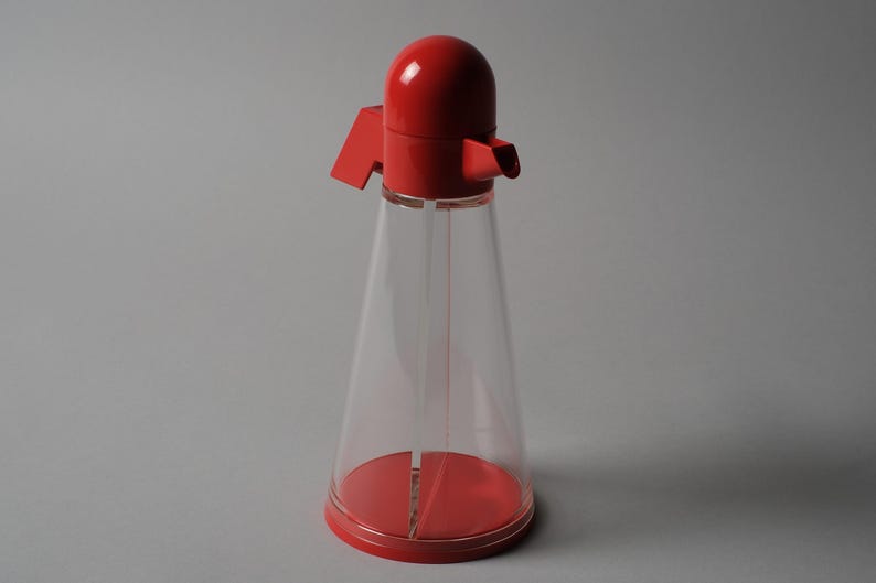 Postmodern Clarity. This second image provides a direct front view of the Bicondi cruet, highlighting the sharp contrast between the clear conical reservoir and the vibrant red geometric top. The design language is unmistakably 1980s Italian, prioritizing bold shapes and vibrant color palettes while remaining a high-performance kitchen tool.