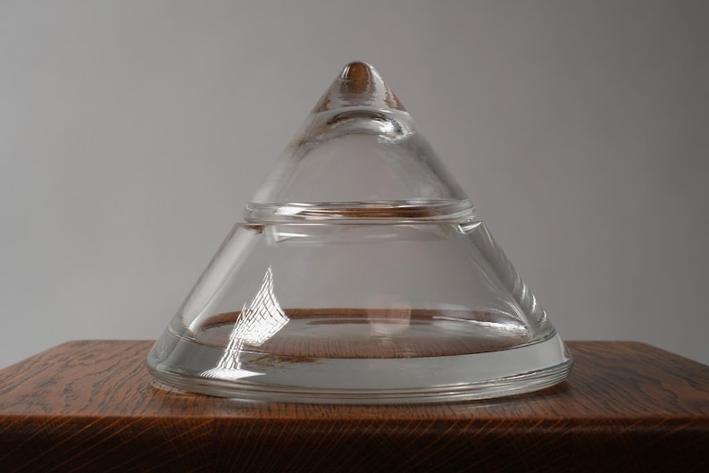 The Pyramidal Form. This first image introduces a striking 1980s crystal glass bonbonnière. This piece is a quintessential example of Postmodern minimalism, stripping away all surface ornamentation to focus entirely on the interplay of light and pure geometric volume. The two-part construction creates a perfect conical silhouette that feels both ancient and futuristic.