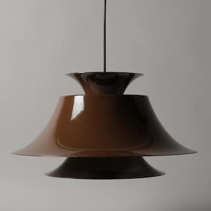 May include: A glossy brown pendant light fixture featuring a multi-tiered design with a wide, flared main shade and a smaller, inverted conical top section. The lamp is suspended by a thin black cord, showcasing a smooth, reflective finish.