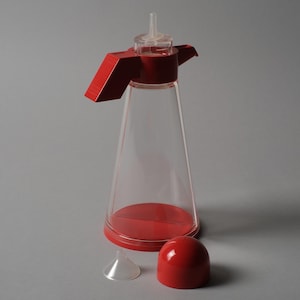 Modular Geometry. This fifth image shows the Bicondi with the red top assembly removed, revealing the clever internal engineering required for a dual-purpose cruet. By separating the components, we see how the designers maintained a minimalist exterior while managing complex functional needs.