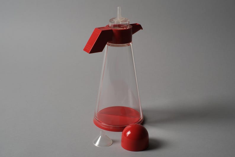 Modular Geometry. This fifth image shows the Bicondi with the red top assembly removed, revealing the clever internal engineering required for a dual-purpose cruet. By separating the components, we see how the designers maintained a minimalist exterior while managing complex functional needs.