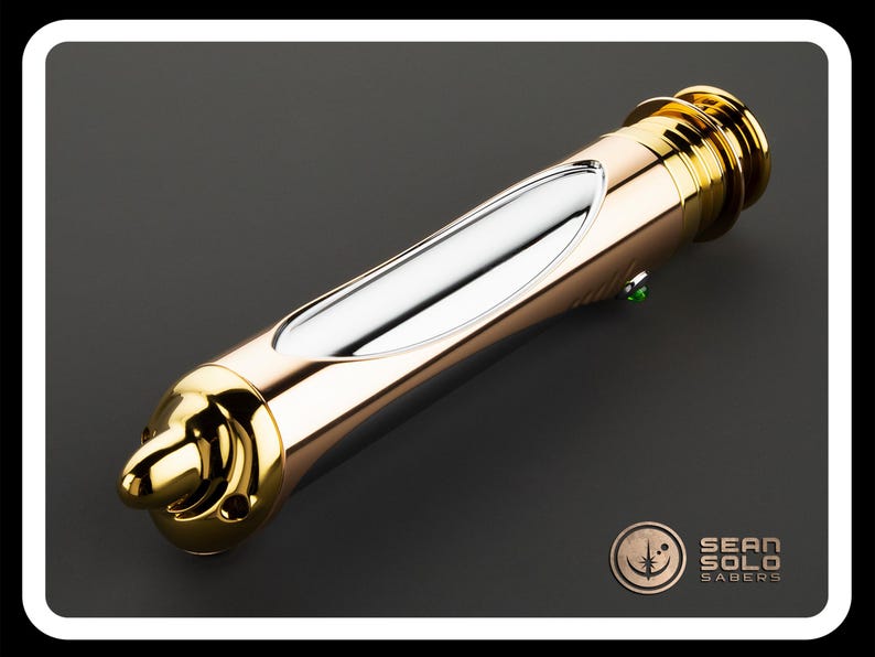 May include: A gold and silver lightsaber with a green button. The lightsaber has a sleek design with a metallic finish. The product is from Sean Solo Sabers.