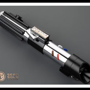 Op de afbeelding: Een zwart en zilveren lightsaber met een zilveren handvat en een zwarte blade. Het handvat heeft een zilveren knop en een zilveren ring. De blade is verlicht met een wit licht. De lightsaber staat op een grijze achtergrond. Sean Solo Sabers.