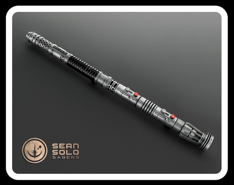 May include: A metallic silver lightsaber hilt with a long, cylindrical body featuring intricate perforated patterns, ribbed sections, and two small red circular buttons. The hilt includes a logo with the text SEAN SOLO SABERS in the corner.
