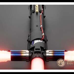 May include: A red lightsaber with a black and silver hilt. The lightsaber is ignited and the blade is red. The hilt has a black handle with a silver band and a silver button. The lightsaber is on a black background.