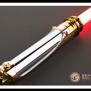 May include: A lightsaber with a polished silver and gold hilt, featuring a red glowing blade. The hilt has a detailed design with a red and green button. The Sean Solo Sabers logo is visible in the bottom right corner.