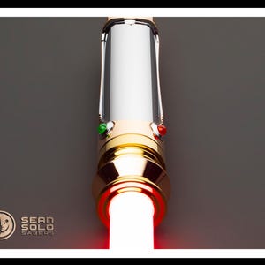 May include: A lightsaber with a gold and silver hilt, featuring a bright red blade. The hilt has green and red buttons. The Sean Solo Sabers logo is in the lower left corner.