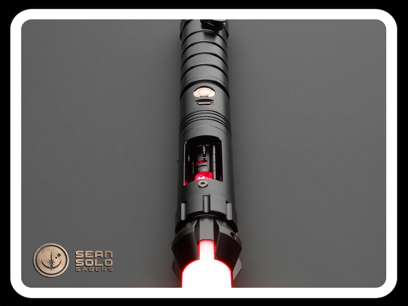 May include: A black lightsaber with a red blade. The lightsaber has a silver button and a black handle with a silver band.