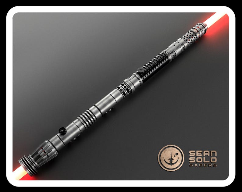 May include: A double-bladed lightsaber with a metallic silver and black hilt featuring intricate cutouts, ribbed sections, and two black activation switches. The blade emits a bright red glow from both ends. The Sean Solo Sabers logo is visible.
