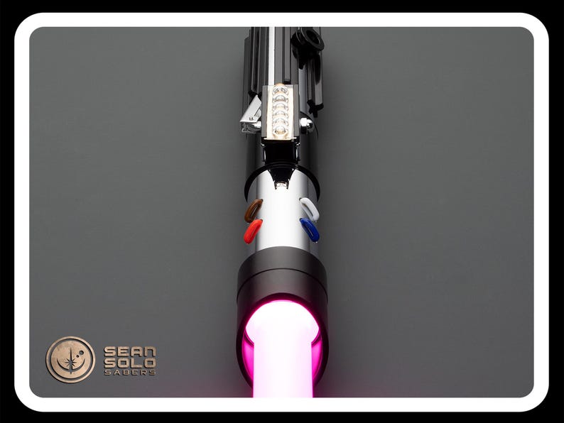 Op de afbeelding: Een zwart lightsaber met een roze blade. De lightsaber heeft een zilveren handvat met een zwarte grip en een zilveren emitter. De lightsaber is aan en de blade gloeit roze.