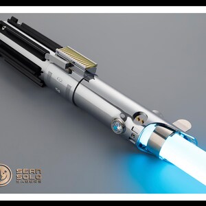 Puede incluir: Un sable de luz plateado con una hoja azul brillante. El mango presenta detalles en negro y plata, con una secci&oacute;n dorada en la parte superior. El logotipo de Sean Solo Sabers est&aacute; en la esquina inferior izquierda.