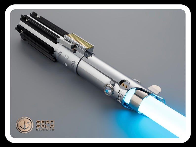 Puede incluir: Un sable de luz plateado con una hoja azul brillante. El mango presenta detalles en negro y plata, con una secci&oacute;n dorada en la parte superior. El logotipo de Sean Solo Sabers est&aacute; en la esquina inferior izquierda.