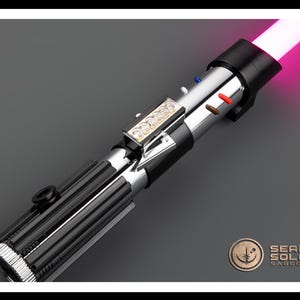 Op de afbeelding: Een zwart en zilveren lightsaber met een roze blade. De lightsaber heeft een zilveren handvat met een zwarte grip en een zilveren emitter. De blade is verlicht en is roze van kleur. De lightsaber is een populair speelgoed voor kinderen en volwassenen.