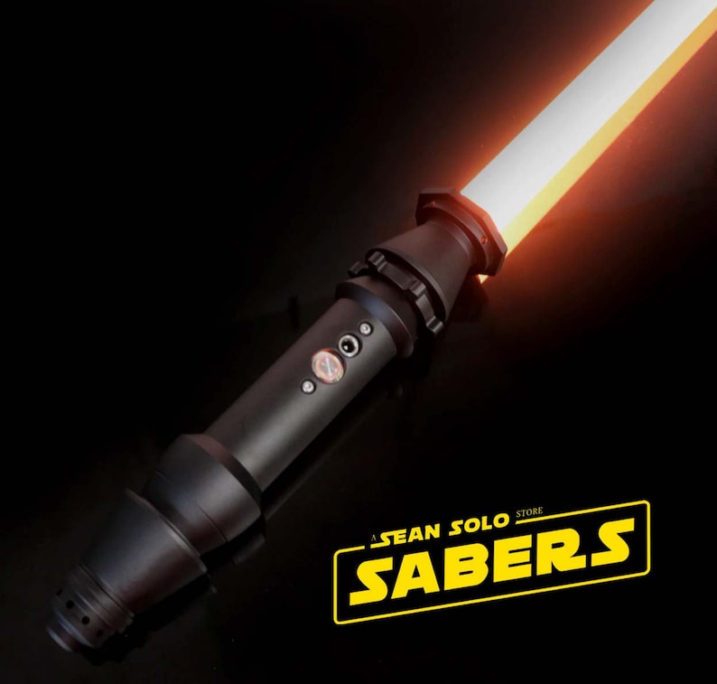 Może przedstawiać: Czarna rękojeść miecza świetlnego z czerwoną klingą. Rękojeść ma fakturowaną powierzchnię i srebrny przycisk. Klinga jest zapalona i świeci. Obraz zawiera r&oacute;wnież tekst "A SEAN SOLO STORE SABERS".
