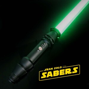 Może przedstawiać: Czarny miecz świetlny z zielonym ostrzem. Miecz świetlny ma czarną rękojeść z srebrnym przyciskiem i srebrnym pokrętłem. Ostrze jest włączone i świeci na zielono. Miecz świetlny znajduje się na czarnej powierzchni. Tekst "A SEAN SOLO STORE SABERS" jest w ż&oacute;łtych literach na czarnym tle.
