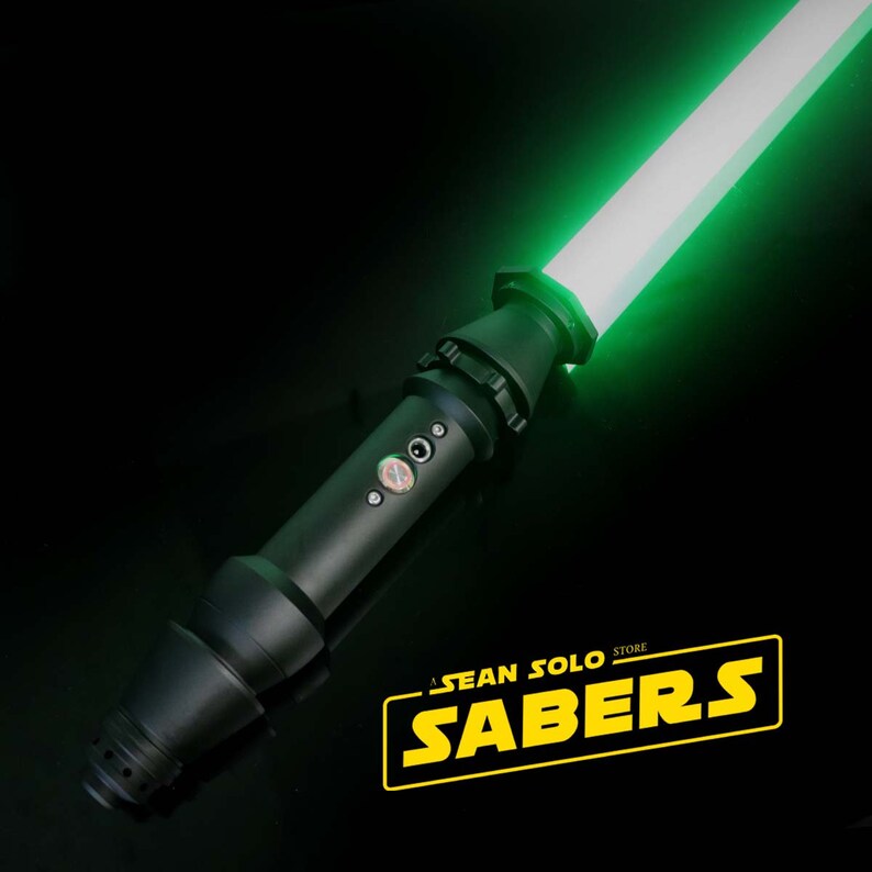 Może przedstawiać: Czarny miecz świetlny z zielonym ostrzem. Miecz świetlny ma czarną rękojeść z srebrnym przyciskiem i srebrnym pokrętłem. Ostrze jest włączone i świeci na zielono. Miecz świetlny znajduje się na czarnej powierzchni. Tekst "A SEAN SOLO STORE SABERS" jest w ż&oacute;łtych literach na czarnym tle.