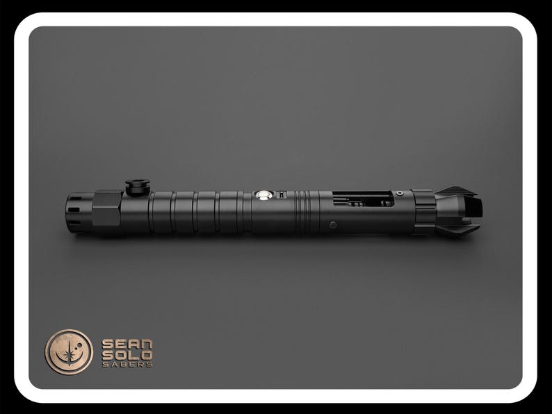 May include: A black lightsaber with a silver button and a black handle. The lightsaber is on a gray surface.