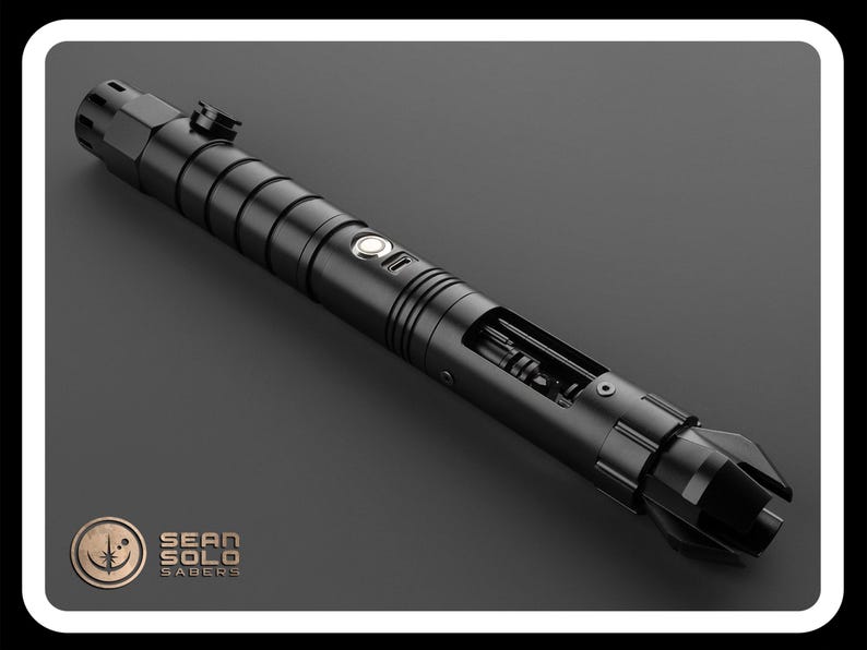 May include: A black lightsaber with a silver button and a partially exposed internal mechanism. The lightsaber is made by Sean Solo Sabers.