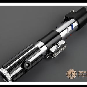 Op de afbeelding: Een zwart en zilveren lightsaber met een blauw en rood licht op de handgreep. De lightsaber is een replica van die gebruikt door Luke Skywalker in de Star Wars-films.