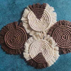 Pode incluir: Quatro  costas de croch&ecirc; feitos &agrave; m&atilde;o com um esquema de cores marrom e branco. Os  costas t&ecirc;m uma borda de franja e s&atilde;o feitos com um padr&atilde;o em espiral.