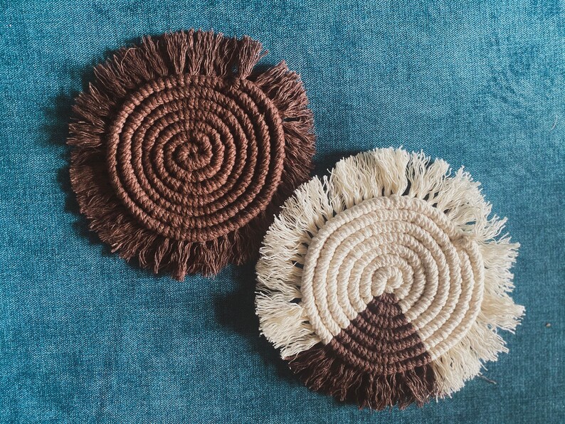 Pode incluir: Dois tapetes de croch&ecirc; feitos &agrave; m&atilde;o. Um &eacute; castanho com uma borda de franja. O outro &eacute; branco com um design de semic&iacute;rculo castanho e uma borda de franja.