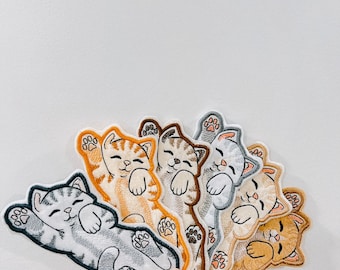 May include: A set of six embroidered iron-on patches featuring cute cartoon cats in various sleeping poses. The patches are in shades of gray, brown, and orange.