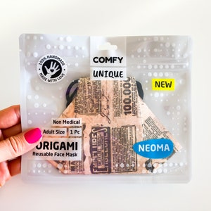 Può includere: Una mascherina origami riutilizzabile in una confezione di plastica trasparente. La mascherina presenta un design con stampa di giornale vintage. La confezione include le parole "Comfy Unique" e "New". La mascherina è etichettata "Non Medical" e "Adult Size".