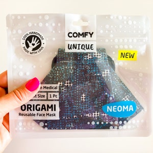 Può includere: Una maschera per il viso Origami riutilizzabile in una confezione di plastica trasparente. La maschera ha un motivo geometrico nelle tonalità del blu, del viola e del bianco. La confezione include il testo "COMFY UNIQUE", "NEW" e "NEOMA". La confezione dice anche "100% HANDMADE MADE WITH LOVE".