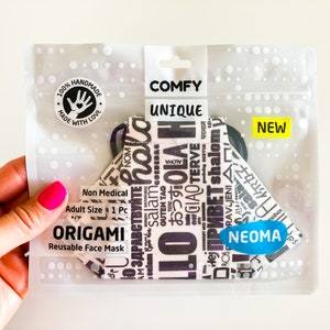 Può includere: Una mascherina facciale origami riutilizzabile in una confezione di plastica trasparente. La mascherina è bianca con testo nero in varie lingue. La confezione riporta le parole "COMFY UNIQUE" e "NEW". La mascherina è etichettata "NEOMA".