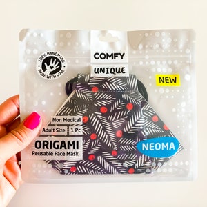 Può includere: Una mascherina facciale origami riutilizzabile in una confezione di plastica trasparente. La mascherina ha uno sfondo nero con un motivo a foglie bianche e bacche rosse. La confezione riporta le parole "COMFY UNIQUE" e "NEW".