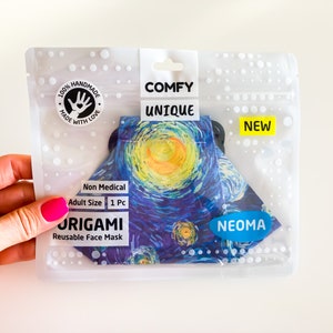 Può includere: Una maschera facciale origami riutilizzabile in una confezione di plastica trasparente. La maschera presenta un design a notte stellata con colori blu, giallo e bianco. La confezione ha le parole "COMFY UNIQUE" e "NEW". Taglia adulti.