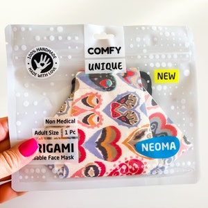 Può includere: Una mascherina per il viso in una confezione di plastica trasparente. La mascherina presenta un motivo paisley con dettagli rossi, blu e arancioni. La confezione riporta le parole "COMFY" e "UNIQUE", insieme alla parola "NEW". Il marchio "NEOMA" è visibile.