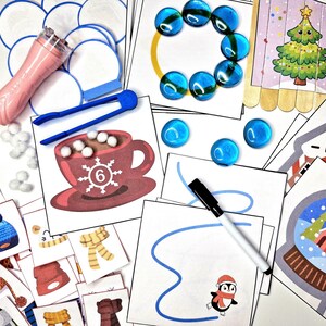 May include: A set of winter-themed educational activity cards for kids. The cards feature images of a snowman, a penguin, a hot chocolate mug, a Christmas tree, and a snow globe. The cards are designed to help children learn about winter and the holidays.