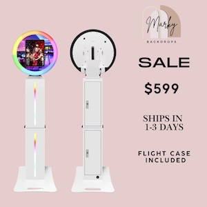 May include: Two white photo booth kiosks with ring lights. The left unit shows a front view with a tablet screen displaying a group photo and a rainbow-coloured LED ring. The right unit shows the back view with a flat circular panel and a tall stand.