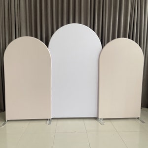 May include: Three arched panels for a backdrop, one white and two beige. The panels are freestanding and have a simple, modern design.