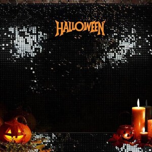May include: A Halloween display with a black backdrop and the word "HALLOWEEN" in orange. The scene includes lit candles, carved pumpkins, and foliage, creating a festive atmosphere. The backdrop is set against a brick wall.